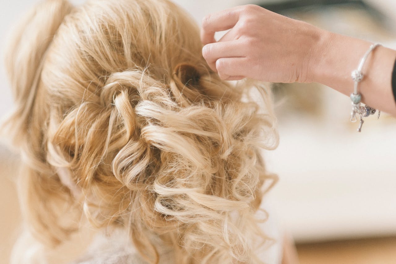 A professional hairstylist creates a blonde bridal updo for a wedding.